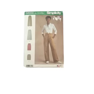 May include: Simplicity sewing pattern S8956 featuring a woman wearing tan wide-leg pants and a white button-down shirt. The pattern includes illustrations of different pant styles in various colors. The pattern's packaging is green and white.