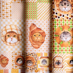 May include: A fabric with a repeating pattern of cats wearing different types of bread. The cats are illustrated in a cartoon style with large eyes and are wearing bread such as croissants, baguettes, and loaves of bread. The fabric is a light beige color with a checkered pattern.