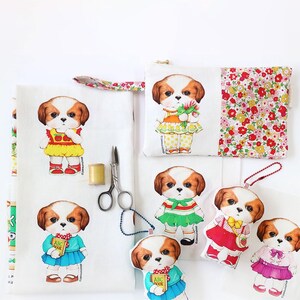Pode incluir: Um tecido branco com um padr&atilde;o repetido de um c&atilde;o de desenho animado vestindo diferentes roupas. O c&atilde;o est&aacute; vestindo um vestido amarelo com uma ma&ccedil;&atilde; vermelha, um vestido verde com uma faixa vermelha e branca, um vestido azul com um "ABC Book", um vestido vermelho com um morango e um vestido rosa com um la&ccedil;o. H&aacute; tamb&eacute;m uma pequena bolsa com um design de c&atilde;o semelhante e um padr&atilde;o floral nas costas.