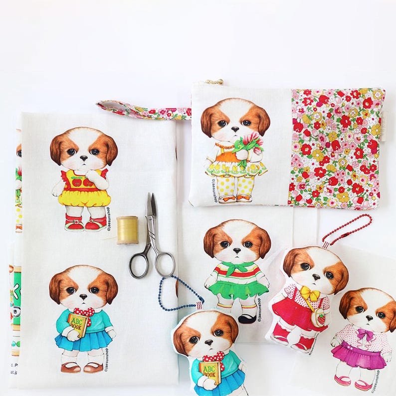 Pode incluir: Um tecido branco com um padr&atilde;o repetido de um c&atilde;o de desenho animado vestindo diferentes roupas. O c&atilde;o est&aacute; vestindo um vestido amarelo com uma ma&ccedil;&atilde; vermelha, um vestido verde com uma faixa vermelha e branca, um vestido azul com um "ABC Book", um vestido vermelho com um morango e um vestido rosa com um la&ccedil;o. H&aacute; tamb&eacute;m uma pequena bolsa com um design de c&atilde;o semelhante e um padr&atilde;o floral nas costas.