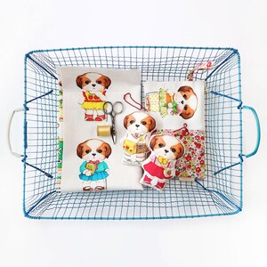 Pode incluir: Uma cesta de arame azul cheia de retalhos de tecido e brinquedos de pel&uacute;cia. Os brinquedos s&atilde;o todos c&atilde;es vestindo roupas diferentes. Os retalhos de tecido s&atilde;o impressos com padr&otilde;es florais e uma cena escolar.