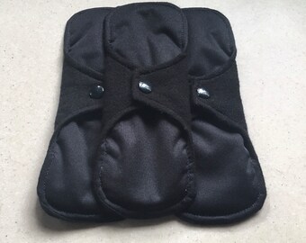 May include: Three black reusable cloth menstrual pads with snap closures.