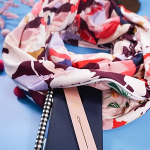 May include: A blue phone case with the word "Brave" printed on it, a pink nail file with a gold needle design, a black and white pen, and a pink beaded bracelet on a blue background.