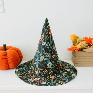 May include: A black witch hat with a floral print. The hat has a tall, pointed cone and a wide brim. The floral print features a variety of flowers and leaves in shades of orange, pink, and green.