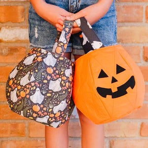 May include: Two Halloween-themed treat bags. One bag is orange and shaped like a jack-o'-lantern with a black face. The other bag is black with a white ghost and pumpkin pattern. Both bags have matching patterned handles.
