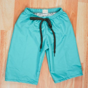 May include: Teal blue swim shorts with a black drawstring. The shorts have a small white label with the word "COOL" on it.