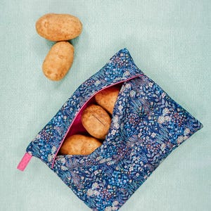 May include: A blue and white floral reusable produce bag with a pink zipper. The bag is filled with four brown potatoes.