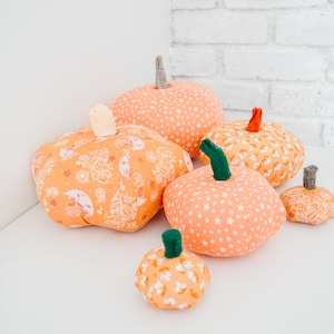 May include: Five orange fabric pumpkins of varying sizes with different patterns. The pumpkins are on a white surface.