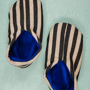 May include: A pair of black and beige striped slippers with blue lining. The slippers are made of a soft, comfortable fabric and have a cozy feel.