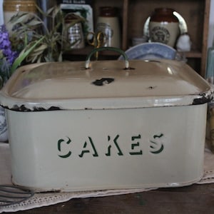 May include: A vintage white enamel cake tin with a green lid and the word "CAKES" written in green lettering on the front.