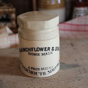 May include: An antique cream-coloured ceramic jar with a matching lid. The jar has black text reading "Blanchflower & Son" and "Home Made". It also states "4 Prize Medals Yarmouth, Norfolk".