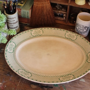 Puede incluir: Un plato ovalado blanco para servir con un diseño floral verde y blanco. El plato está sobre una mesa de madera.
