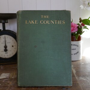 Könnte beinhalten: Ein grünes Hardcover-Buch mit goldener Aufschrift "THE LAKE COUNTIES".