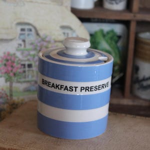 May include: A ceramic breakfast preserve jar with a lid. The jar is cylindrical with alternating horizontal bands of light blue and white. The words "BREAKFAST PRESERVE" are printed in black on the jar.