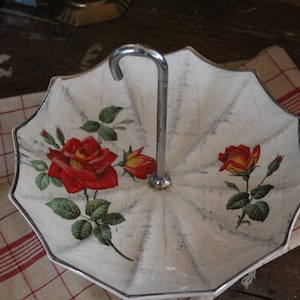 May include: White ceramic umbrella-shaped serving dish with a silver handle. The dish is decorated with red and yellow roses.