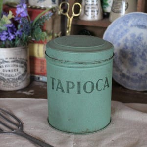 Peut inclure: Une boîte en métal verte avec le mot "Tapioca" imprimé sur le devant. La boîte est posée sur une surface blanche.