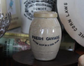 May include: A white ceramic jar with a black label that reads "FRESH CAVIARE PLEASE KEEP IN A COOL PLACE".