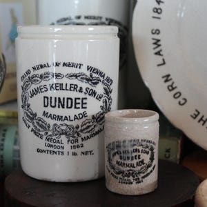 Może przedstawiać: Dwa białe ceramiczne słoiki z czarnym nadrukiem. Większy słoik jest oznaczony napisem "Grand Medal of Merit Vienna 1873 James Keiller & Son Ltd Dundee Marmalade Only Prize Medal for Marmalade London 1862 Contents 1 lb. Net.". Mniejszy słoik jest oznaczony napisem "James Keiller & Son Ltd Dundee Marmalade Only Prize Medal for Marmalade London 1862".