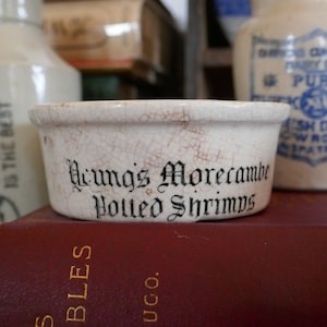 May include: A white ceramic bowl with a cracked glaze and black lettering that reads "Young's Morecambe  Polled Shrimps".