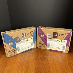 May include: Two cardboard boxes with printed images and text. Each box has a blue and purple stripe, with the text "Happy boys" and "V01-1". The boxes also have small images and shipping labels.
