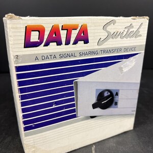 May include: A data switch device in its original packaging. The box features the word "DATA" in gradient orange and purple, with "Switch" in silver. The box also has blue and white stripes and the text "A DATA SIGNAL SHARING/TRANSFER DEVICE".