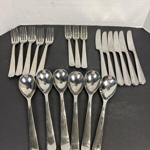 May include: A collection of stainless steel silverware, including forks, knives, and spoons. The silverware is arranged on a dark surface, with the spoons in the foreground. The forks and knives are in the background.