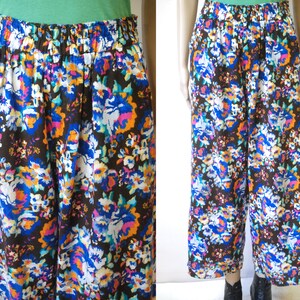 May include: A pair of wide-leg pants with a floral print in shades of blue, orange, pink, and white on a brown background. The pants have an elastic waistband.