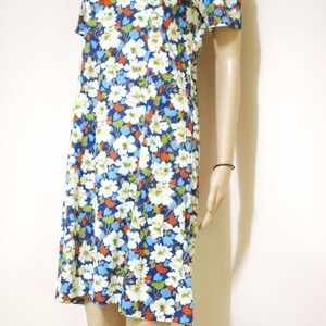 May include: A short-sleeved dress with a floral print in shades of white, blue, orange, and green. The dress has a round neckline and a slightly flared skirt.