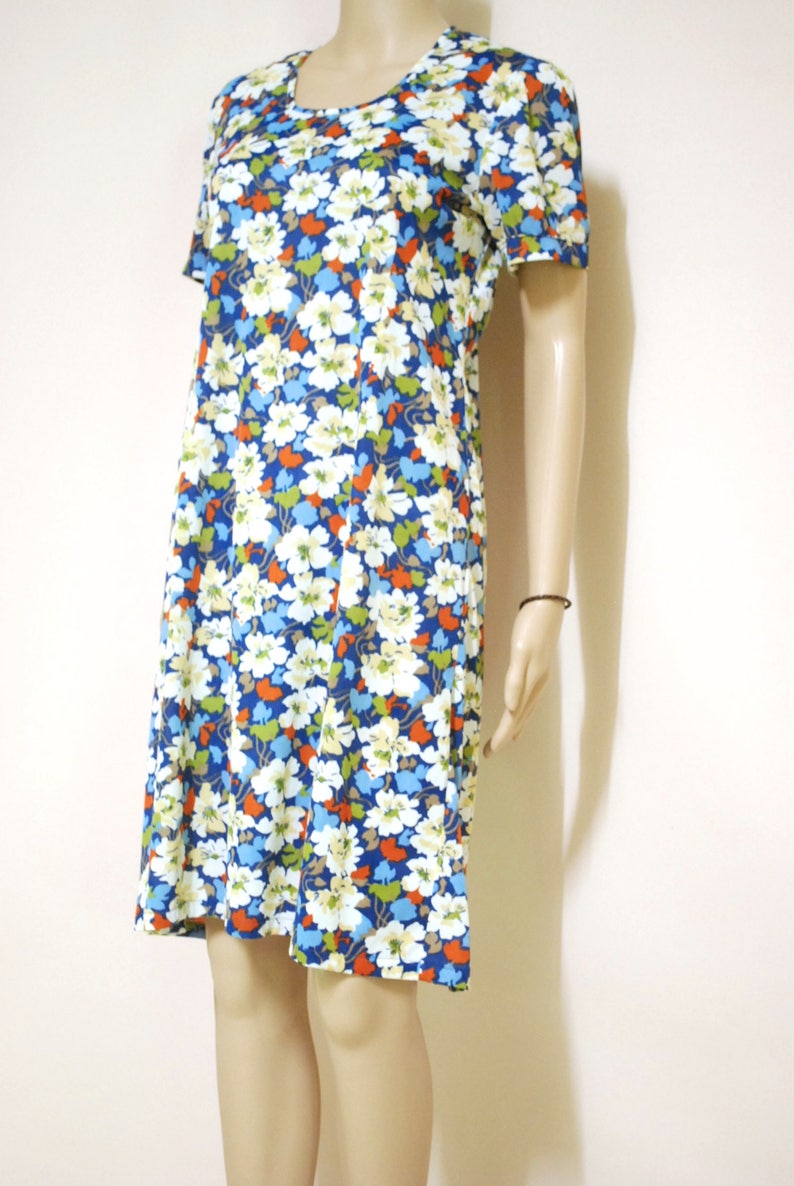 May include: A short-sleeved dress with a floral print in shades of white, blue, orange, and green. The dress has a round neckline and a slightly flared skirt.