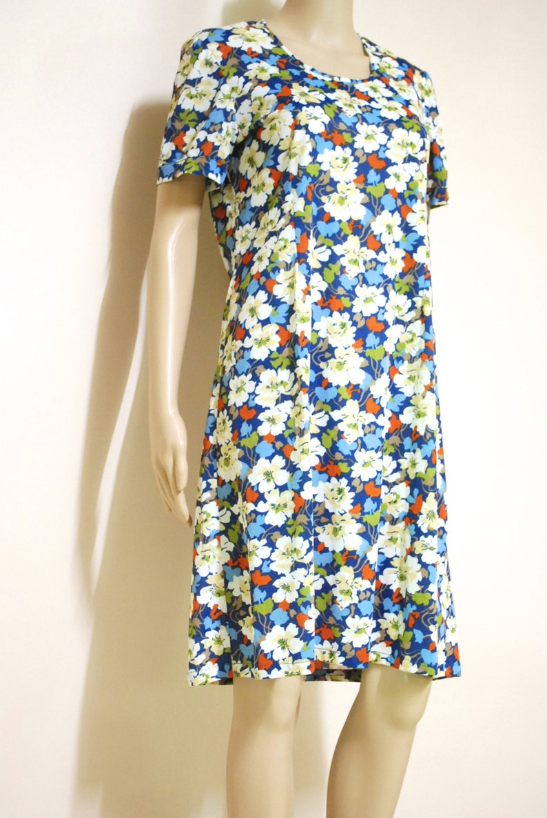 May include: A short-sleeved dress with a floral print in shades of blue, white, orange, and green. The dress has a round neckline and a slightly flared skirt.
