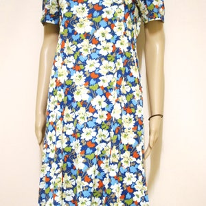 May include: A short-sleeved dress with a floral print in shades of blue, white, orange, and green. The dress has a round neckline and a slightly flared skirt.