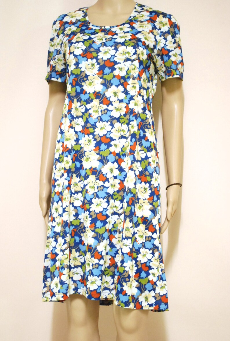 May include: A short-sleeved dress with a floral print in shades of blue, white, orange, and green. The dress has a round neckline and a slightly flared skirt.