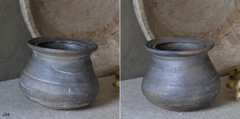 Może przedstawiać: Ciemnoszary, zaokrąglony garnek ceramiczny z szerokim, rozszerzającym się brzegiem i teksturowaną, matową powierzchnią. Naczynie posiada subtelne poziome żłobienia i r&oacute;żnice w odcieniach na korpusie, z głębokim, otwartym wlotem i stabilną podstawą.