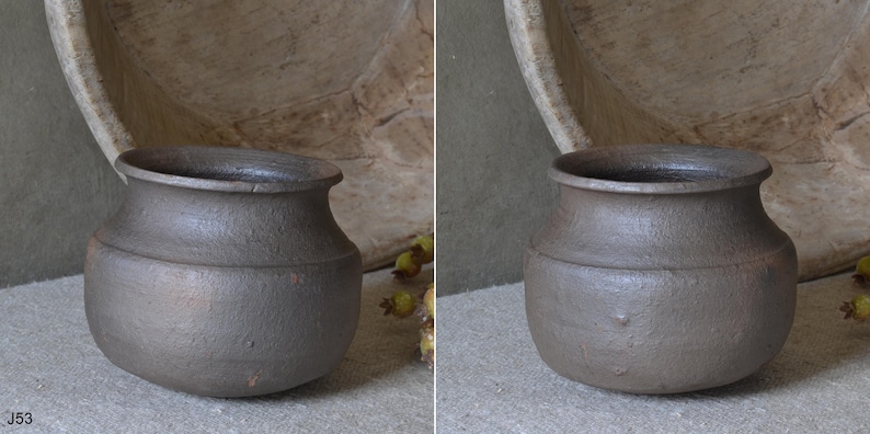 Może przedstawiać: Mały, ciemnobrązowy, zaokrąglony garnek ceramiczny z szerokim, rozszerzającym się brzegiem i teksturowaną, matową powierzchnią. Naczynie posiada wyraźne poziome żebrowanie wok&oacute;ł środkowej części oraz lekko zwężającą się podstawę o prostej formie.