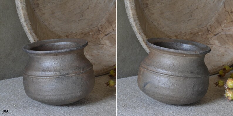 Może przedstawiać: Mały, ciemnoszary ceramiczny garnek o zaokrąglonym korpusie, szerokim otworze i rozszerzanym rancie. Powierzchnia ma teksturowane, matowe wykończenie z subtelnymi r&oacute;żnicami w odcieniach. Garnek posiada poziomą linię wok&oacute;ł środkowej części.