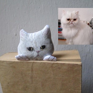 Peut inclure: Un chat en peluche blanc avec une expression boudeuse. Le chat regarde par-dessus le bord d'une bo&icirc;te en carton marron. Le jouet est une repr&eacute;sentation r&eacute;aliste d'un chat persan.