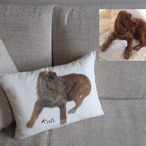 May include: A white pillow with a brown and white dog illustration and the name "Kali" written in black. The pillow is on a beige couch.