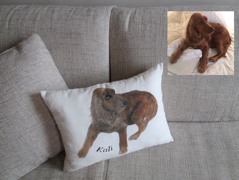 May include: A white pillow with a brown and white dog illustration and the name "Kali" written in black. The pillow is on a beige couch.