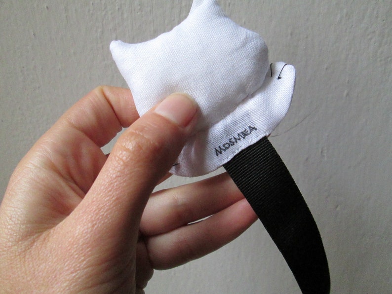 Peut inclure: &Eacute;toile en tissu blanc avec une sangle noire et le mot "MOSMEA" brod&eacute; dessus.