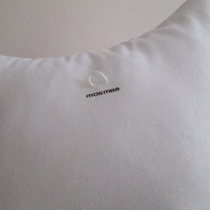 May include: White pillow with a small loop and the word "mosmea" printed on it.
