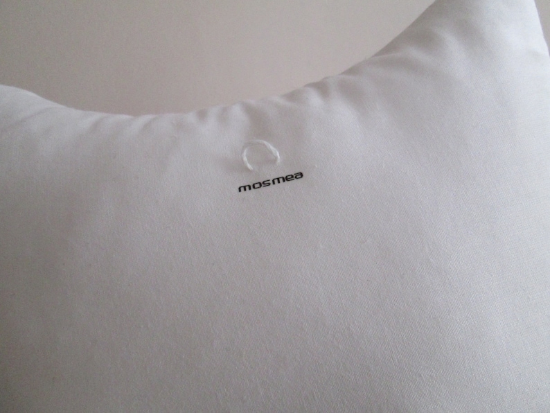 May include: White pillow with a small loop and the word "mosmea" printed on it.