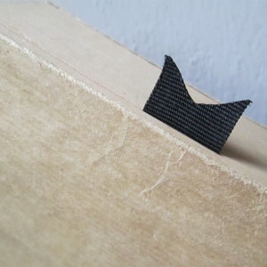 Peut inclure: Gros plan sur une bo&icirc;te en carton beige avec un marque-page en tissu noir attach&eacute; au bord sup&eacute;rieur.