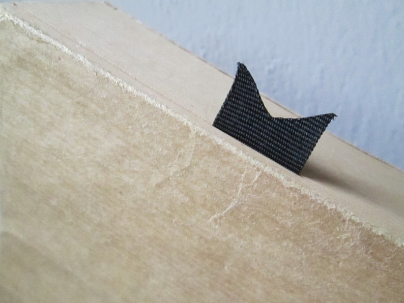 Peut inclure: Gros plan sur une bo&icirc;te en carton beige avec un marque-page en tissu noir attach&eacute; au bord sup&eacute;rieur.
