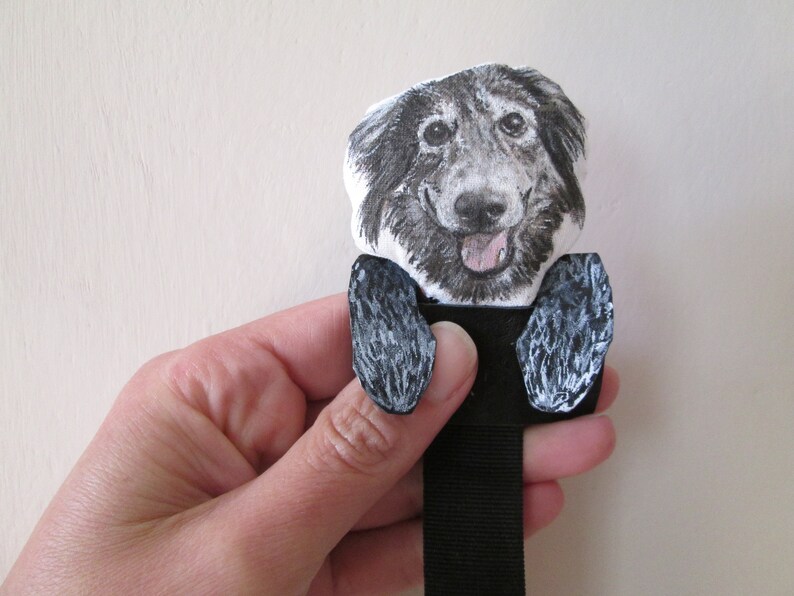 May include: A black and white dog-themed bookmark. The bookmark features a smiling dog face with a pink tongue and two black paws. The dog's face is printed on a white background, and the paws are painted black and white.