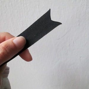 Peut inclure: Un ruban noir avec une extr&eacute;mit&eacute; pointue, tenu dans une main.