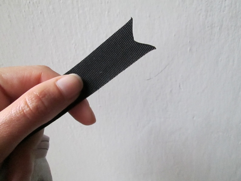 Peut inclure: Un ruban noir avec une extr&eacute;mit&eacute; pointue, tenu dans une main.