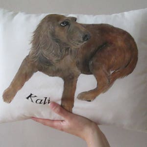 May include: A white pillow with a brown dog painted on it. The dog is looking to the right and the pillow has the name "Kali" written on it.