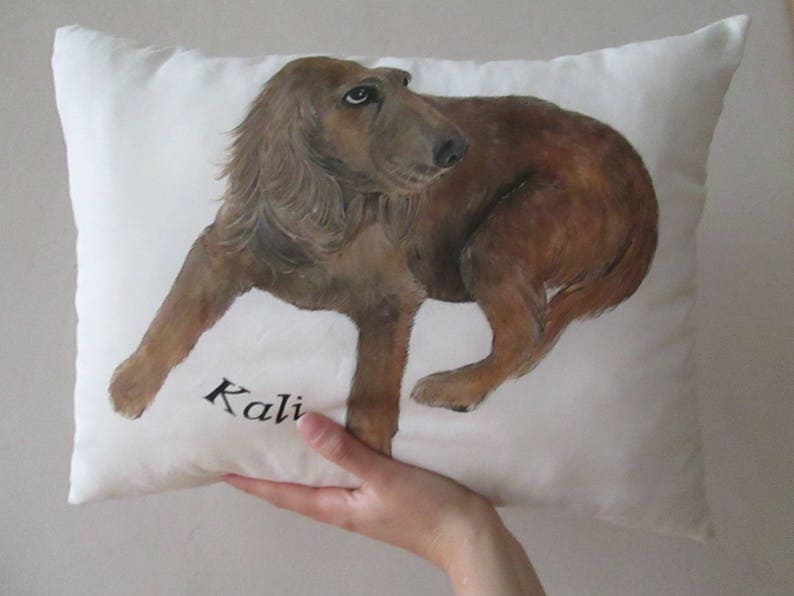 May include: A white pillow with a brown dog painted on it. The dog is looking to the right and the pillow has the name "Kali" written on it.