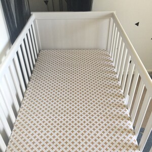 May include: White cot with a gold and white patterned fitted sheet.