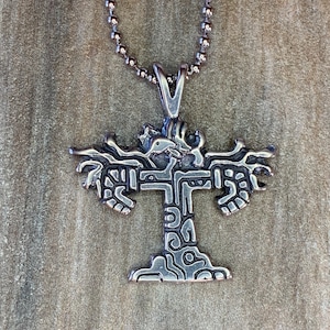 May include: A silver necklace with a pendant shaped like a stylized tree with intricate details. The pendant is made of metal and has a textured surface.